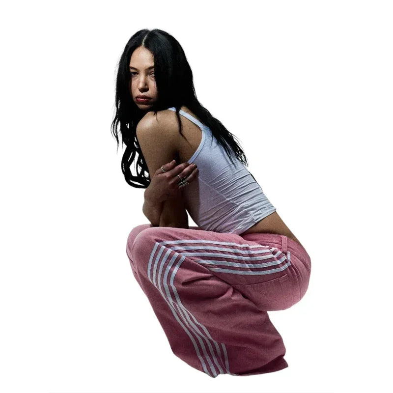 Woman wearing a white tank top and pink sweatpants with white stripes on a white background