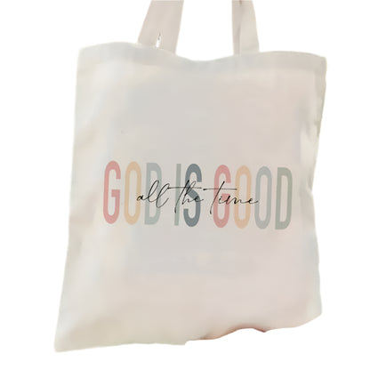 Tote bag with 'GOD IS GOOD all the time' text held by a person against a green background