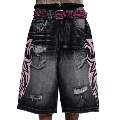 Black denim shorts with pink tribal patterns and a studded belt on a light gray background