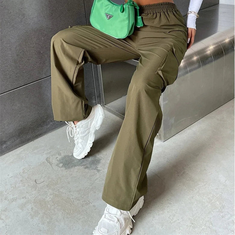 Person wearing a white off-shoulder top and green pants, holding a green bag, sitting on a metallic surface.
