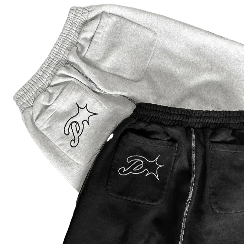 Two pairs of pants, one black and one gray, with embroidered logos on a dark surface.