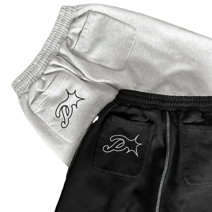 Two pairs of pants, one black and one gray, with embroidered logos on a dark surface.