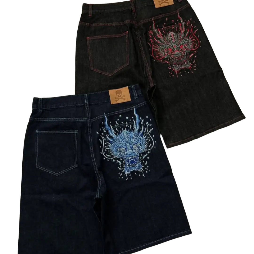 Two pairs of black denim shorts with colorful embroidery on a gray surface