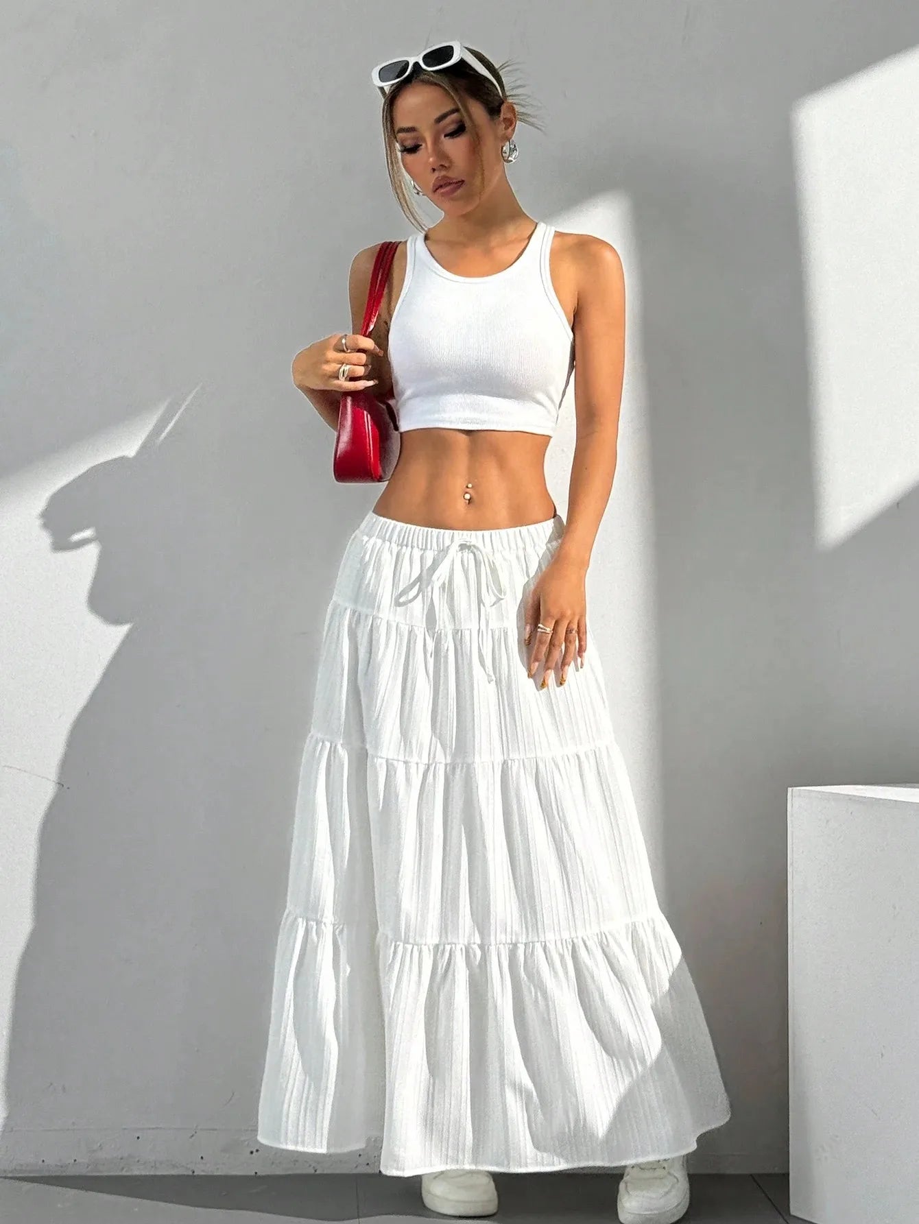 Woman wearing a white outfit with a long skirt against a gray wall.