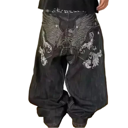 Person wearing black baggy pants with white embroidery on a plain background