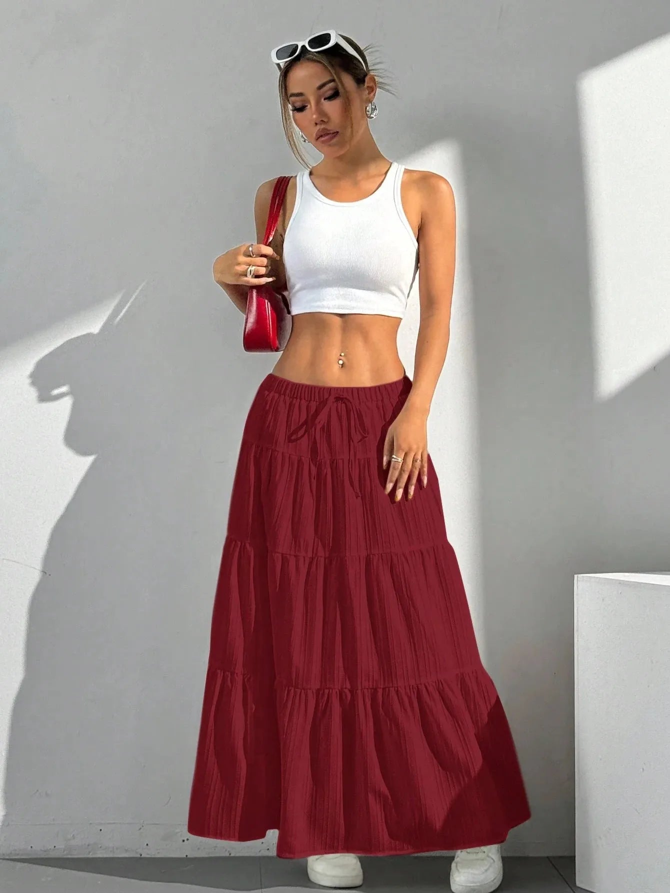 Woman wearing a white crop top and red tiered skirt against a gray wall.